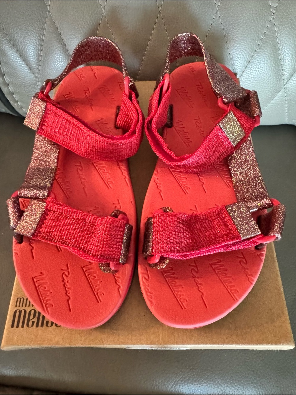 Mini Melissa + Rider sandals feature red, glitter-covered velcro straps.
